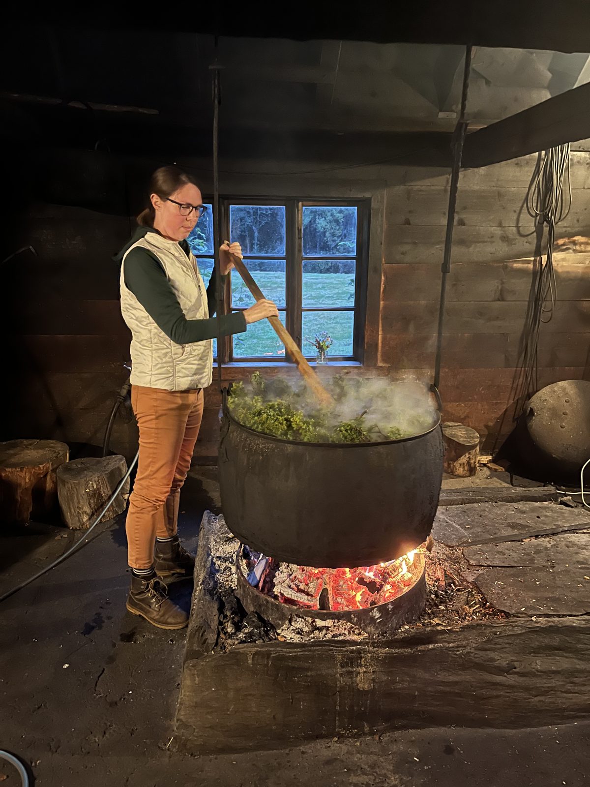 Amanda Thorstad stirring a kettle of juniper wort over an open fire at a Norwegian farmhouse brewery