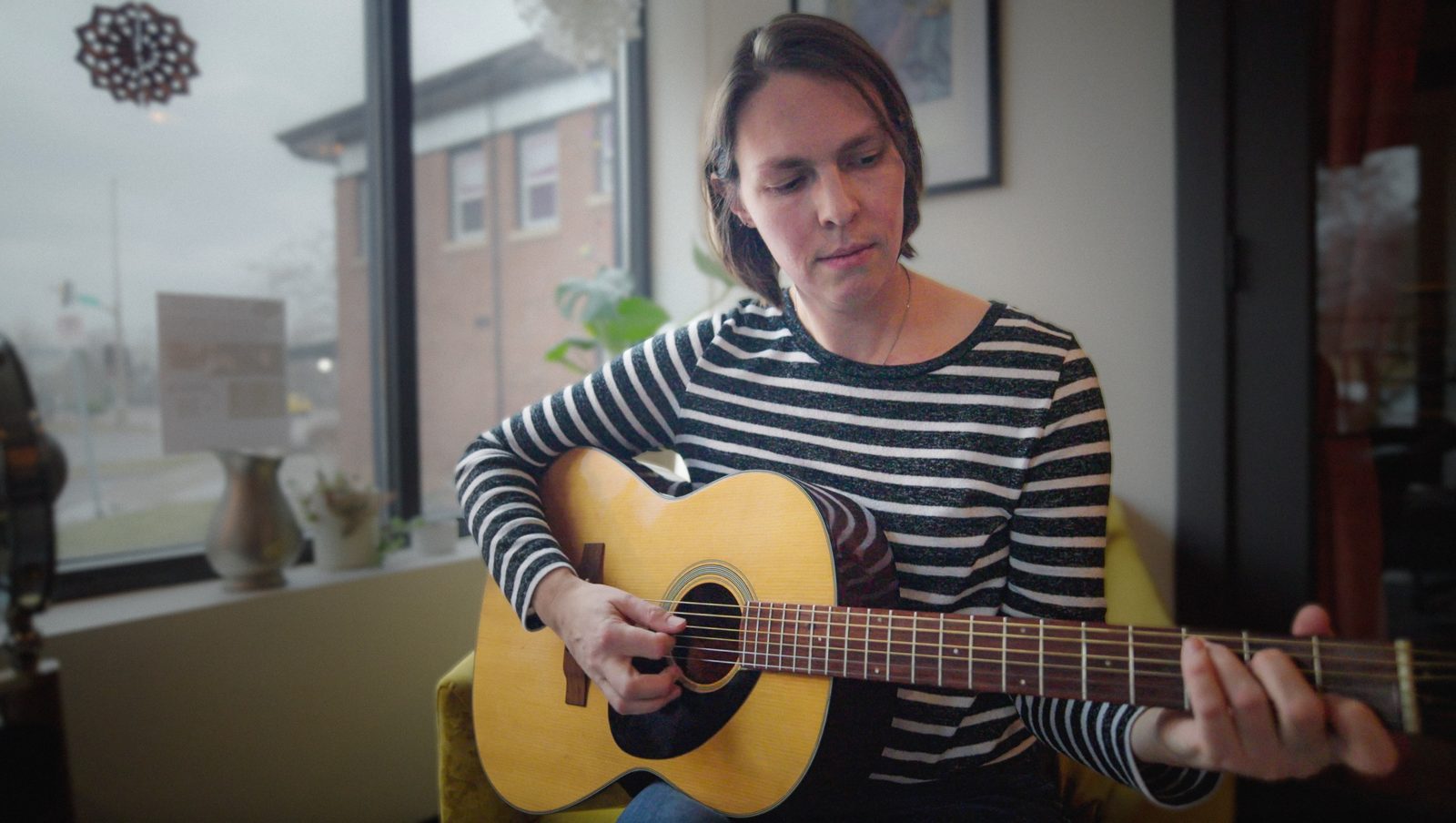 Amanda Thorstad playing acoustic guitar by a window